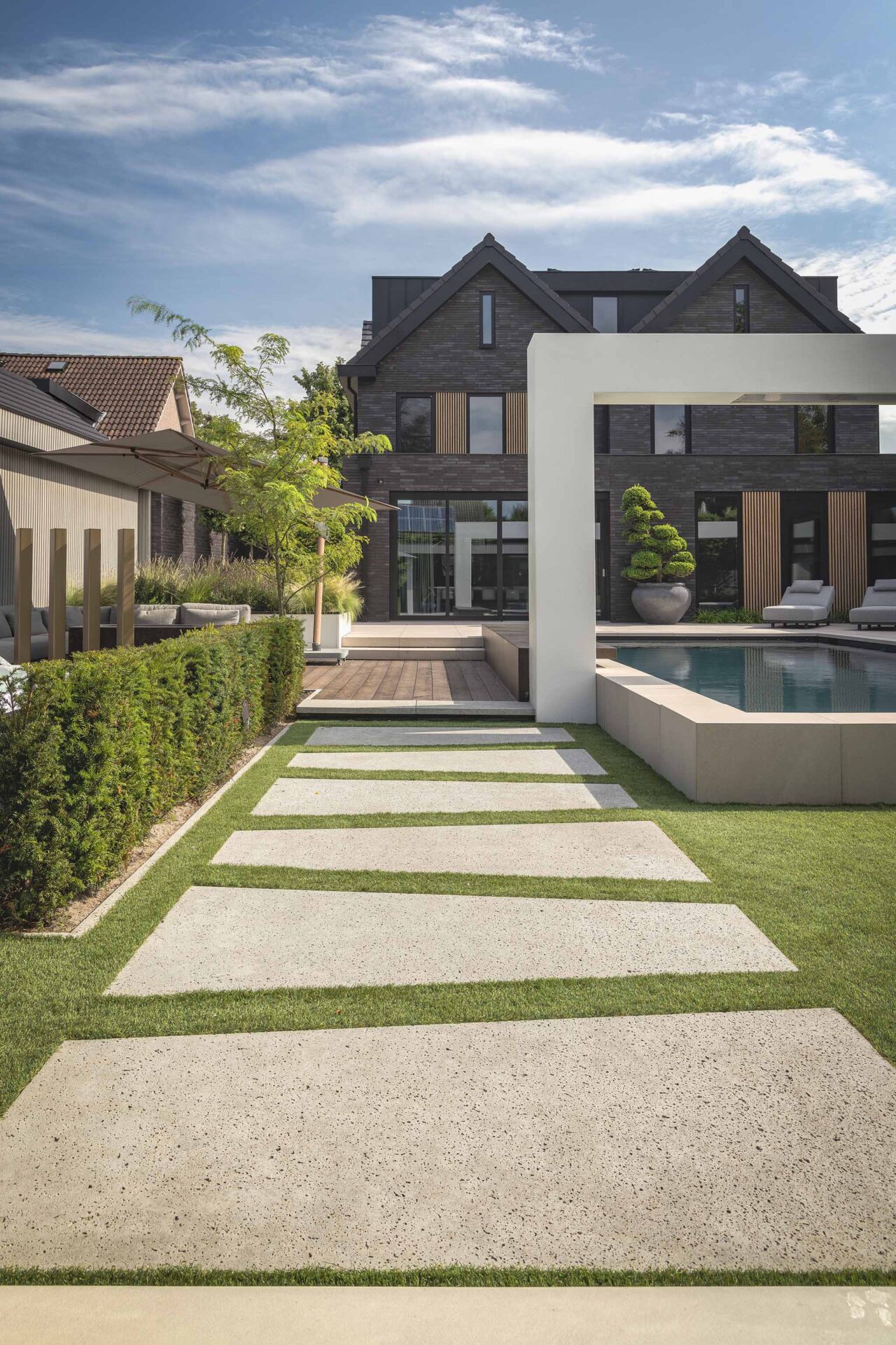 Foto van High End wellnesstuin rosmalen met zicht op grote trapezevormige stapstenen in het gras met op de achtergrond de woning. 