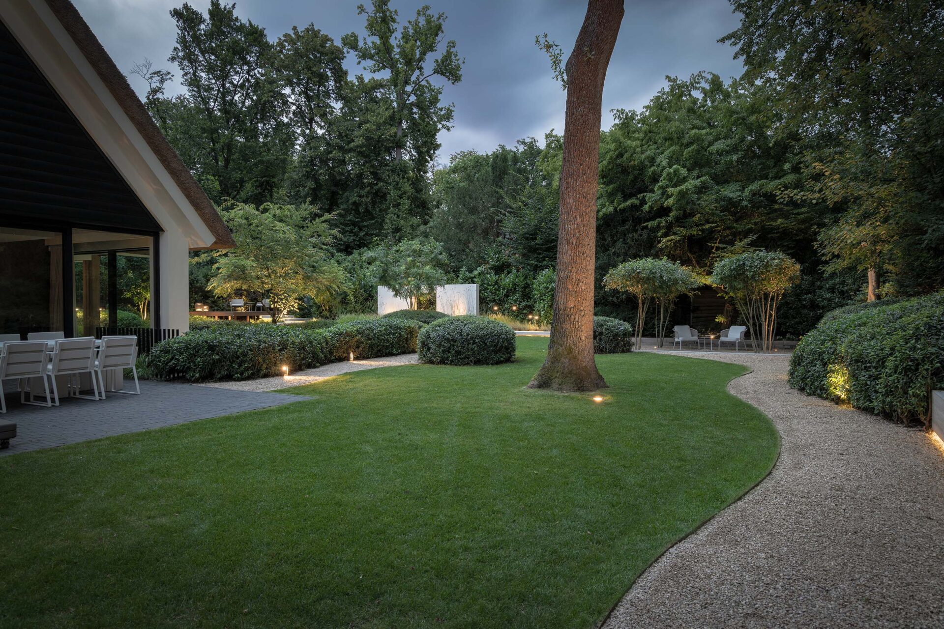 Villatuin Hilversum met zicht op gazon bij schemering en verlichting bij beplanting. 