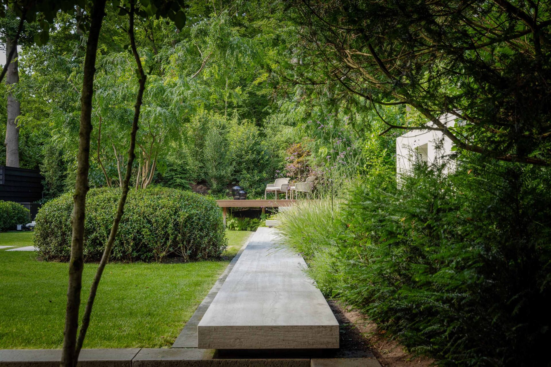 Villatuin Hilversum met zicht over strak recht grijs zitelement als mooi contrast met het omliggende gazon en heesterbeplanting.