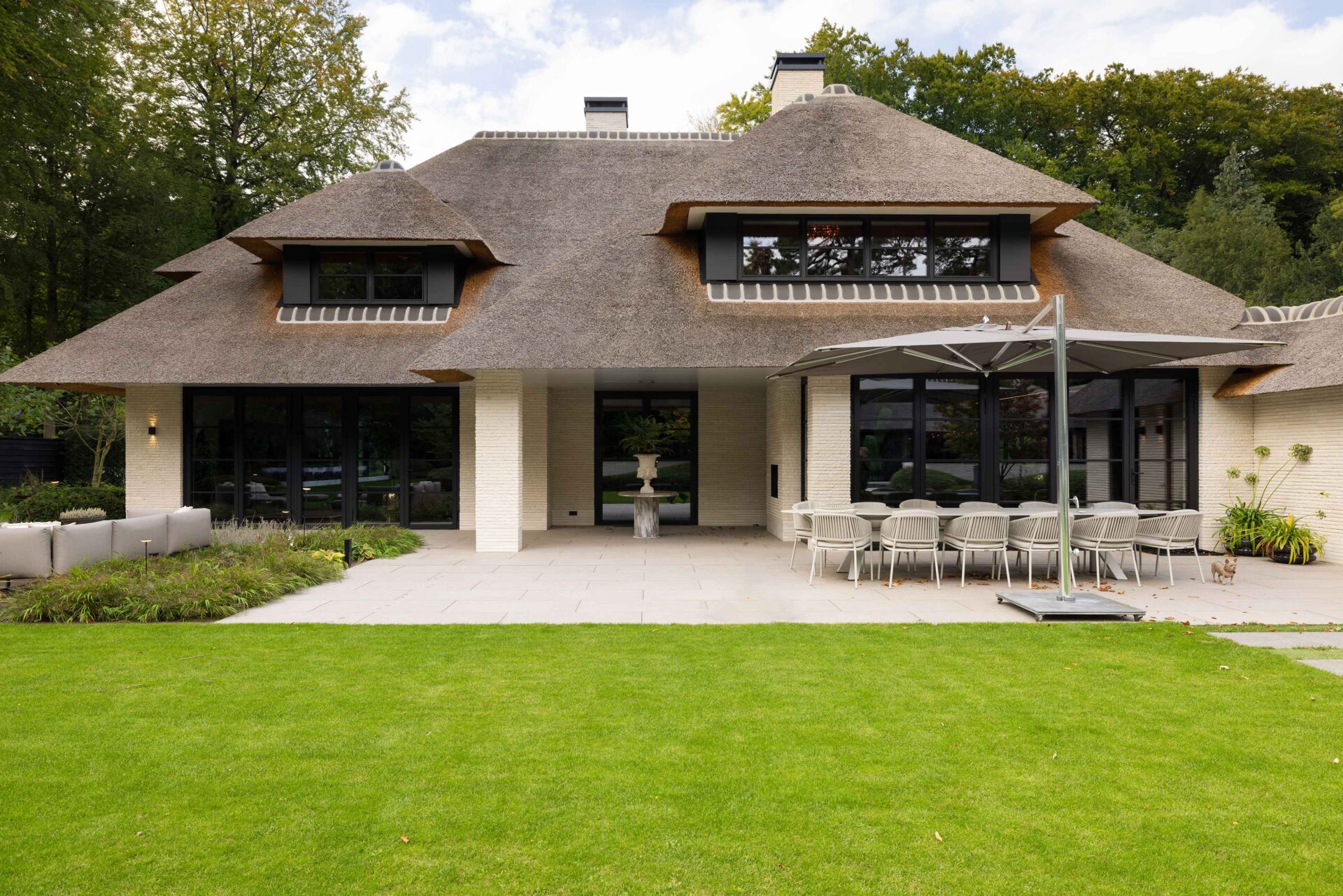 Zicht op de achterzijde van de rietgedekte villa in Blaricum met groot terras en lichte tegels. 