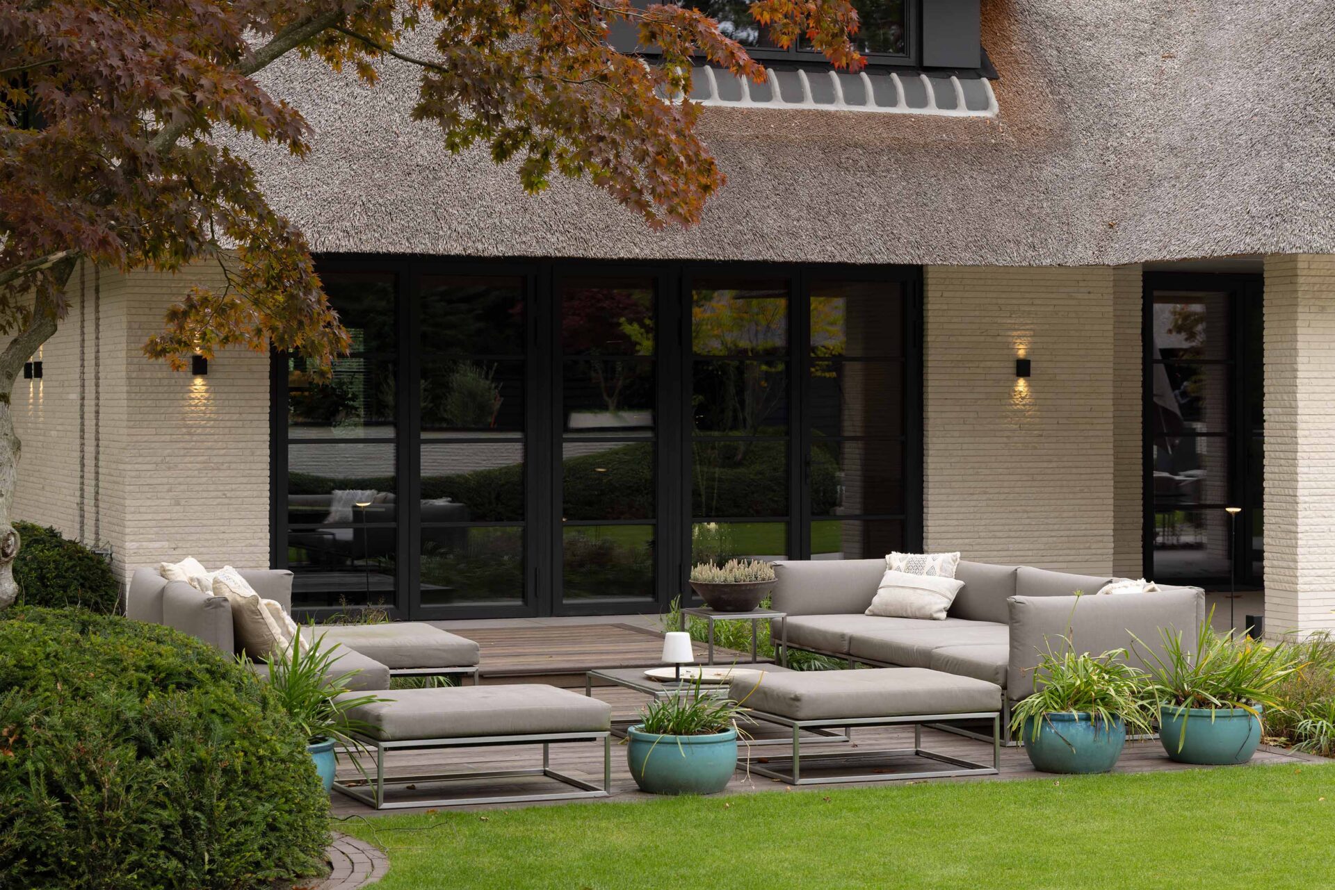 Zicht op zitterras buiten met luxe lounge meubelen direct naast grote raampartij van de villa. 