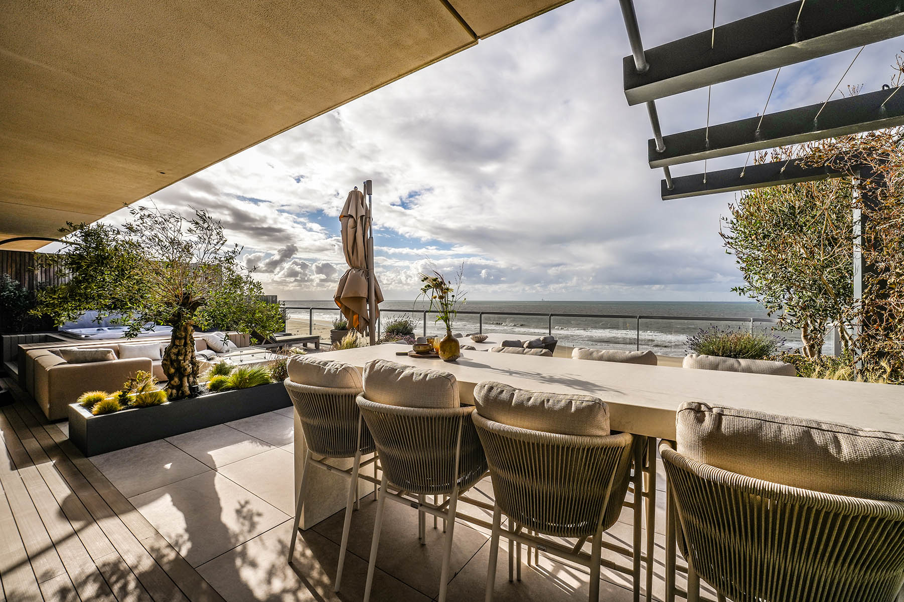 Daktuin Kijkduin met zicht op hoge tafel met stoelen en uitzicht op zee op een zonnige dag. 