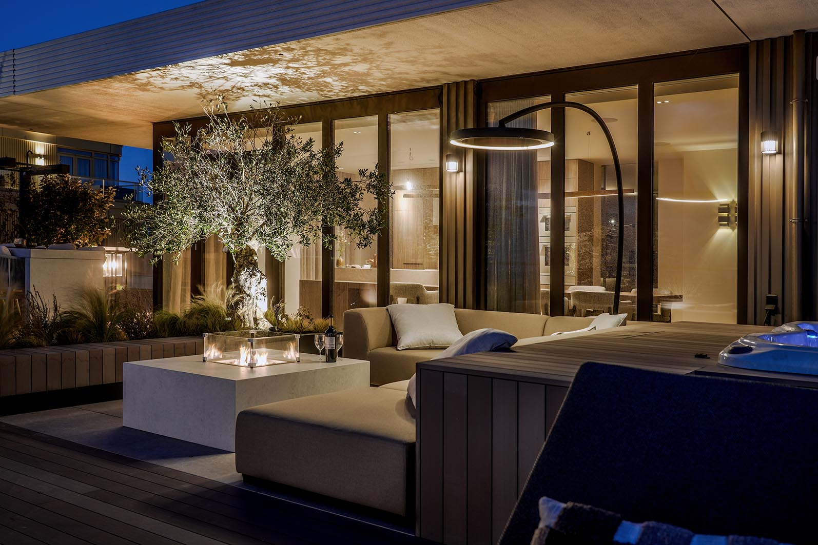 Daktuin Kijkduin in de avond met zicht op de loungehoek met daarachter de glazen pui van de woning en sfeerlicht. 