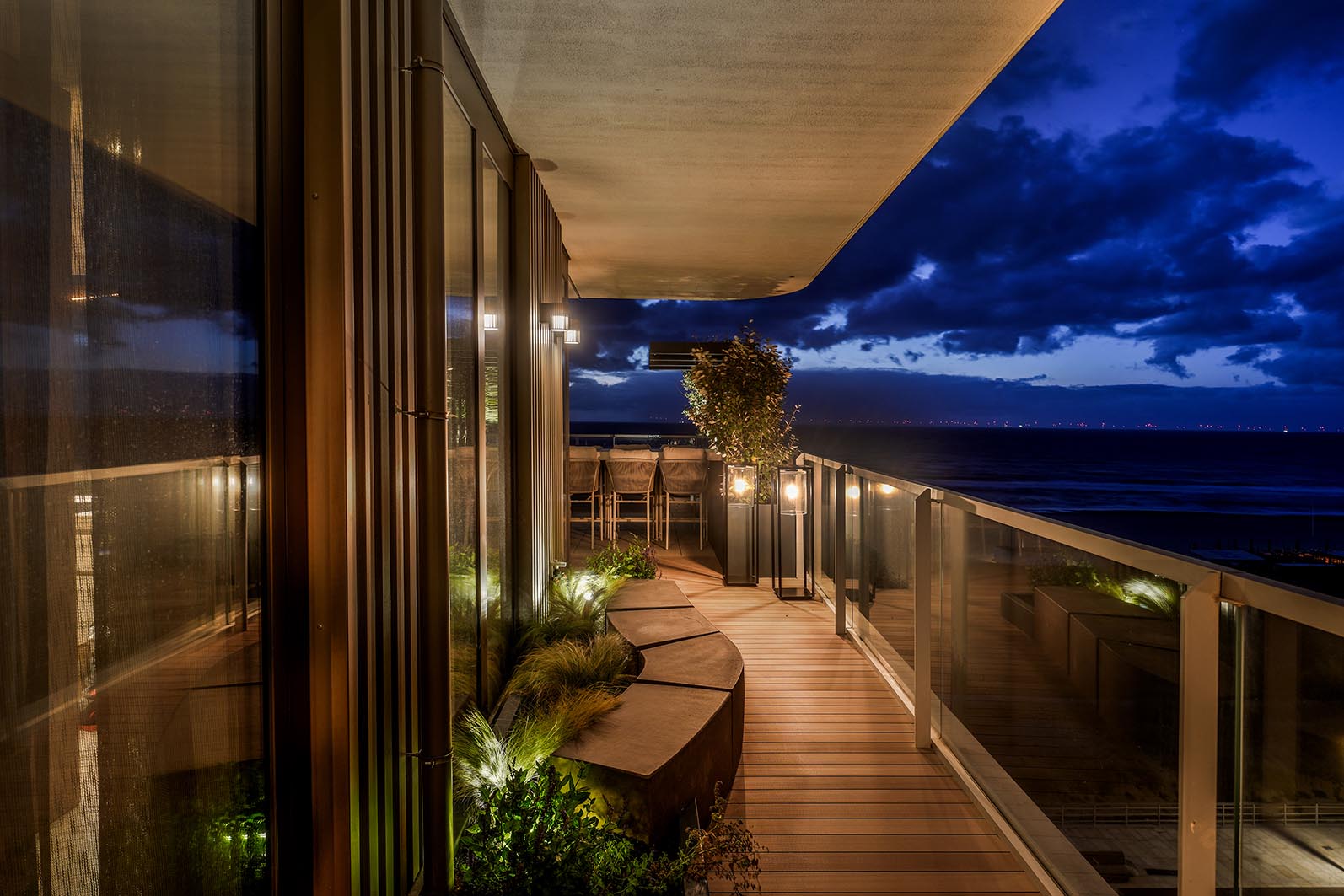 Zicht daktuin Kijkduin, zijkant van dak met zitelementen van beton en beplanting in de avond met sfeerlicht. 