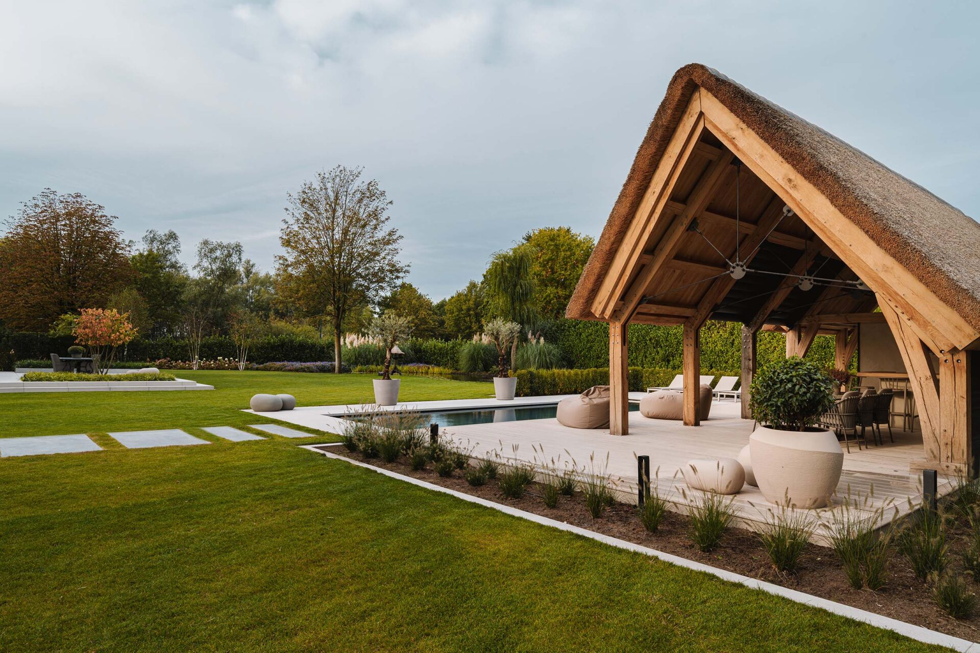 Tuinontwerp Kaatsheuvel van Studio Meulenberg met zicht op de rietgedekte poolhouse en het omliggende gazon.