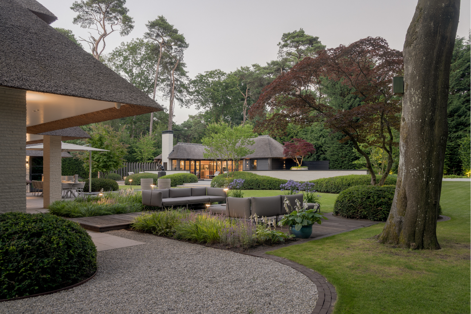 Zicht op zitterras buiten met luxe lounge meubelen direct naast grote raampartij van de villa. 