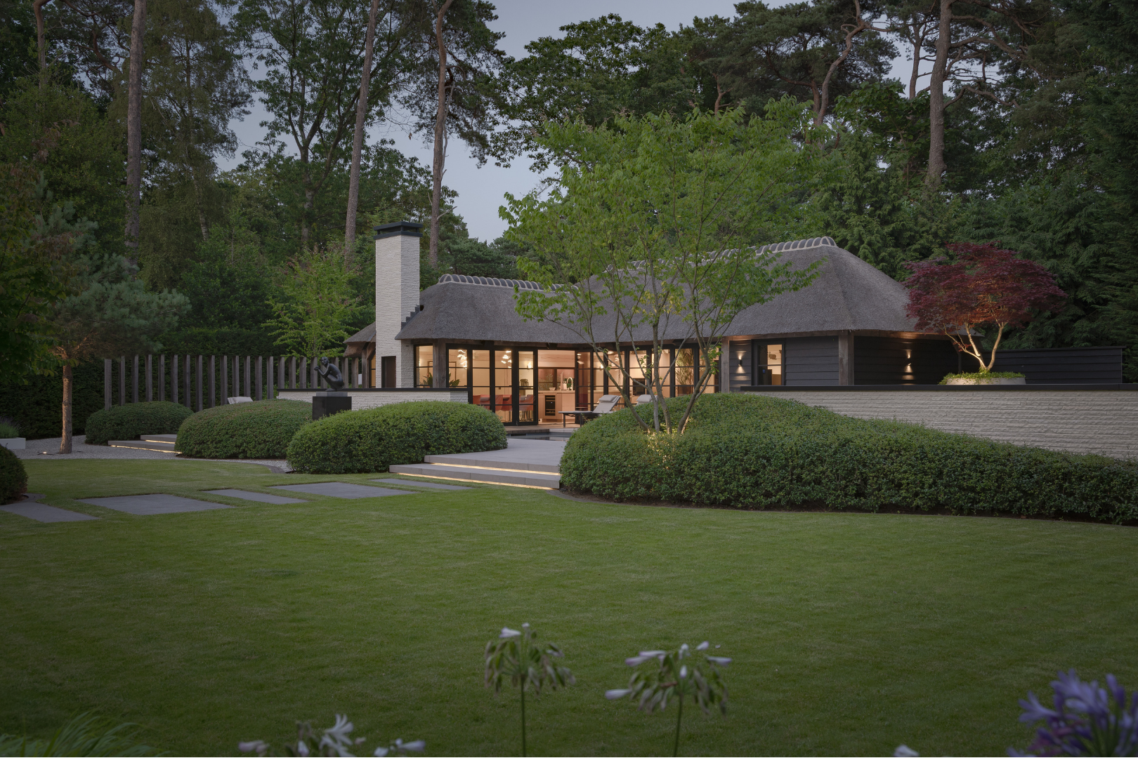 Zicht op de achterzijde van de rietgedekte villa in Blaricum met groot terras en lichte tegels. 