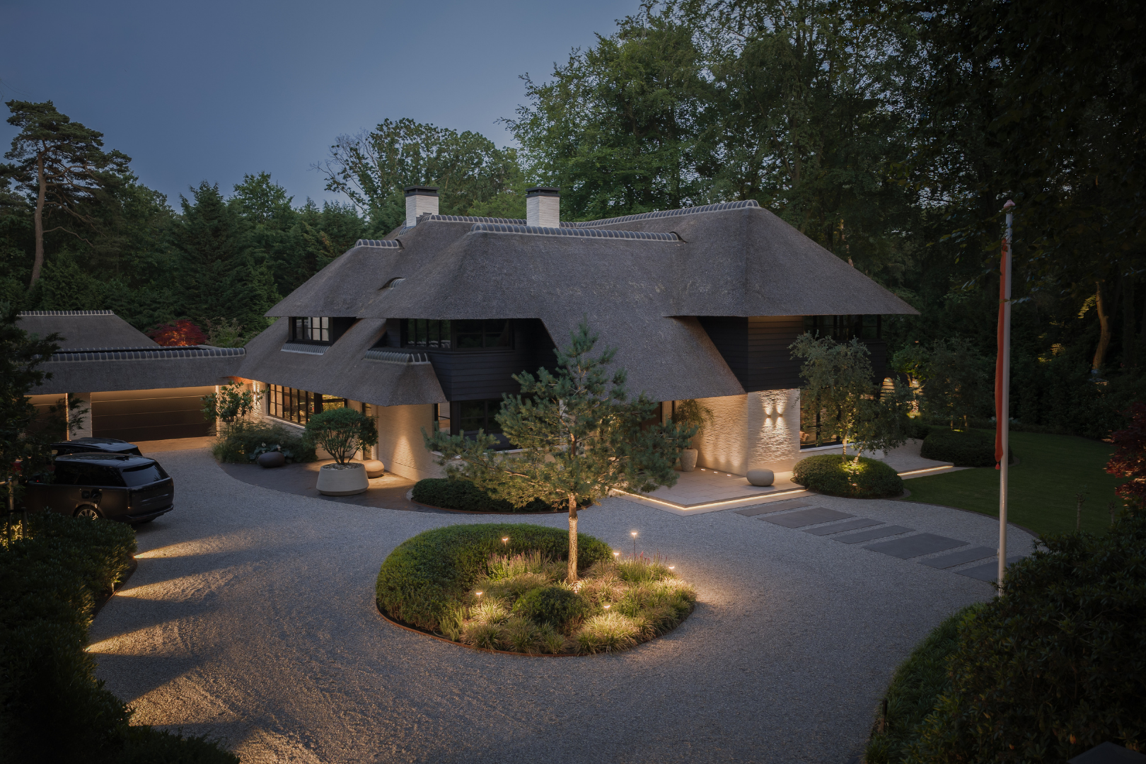 Zicht op de villa te Blaricum in vogelvlucht, rietgedekte villa met groot terras aan de achterzijde met gazon en lichte grote tegels. 